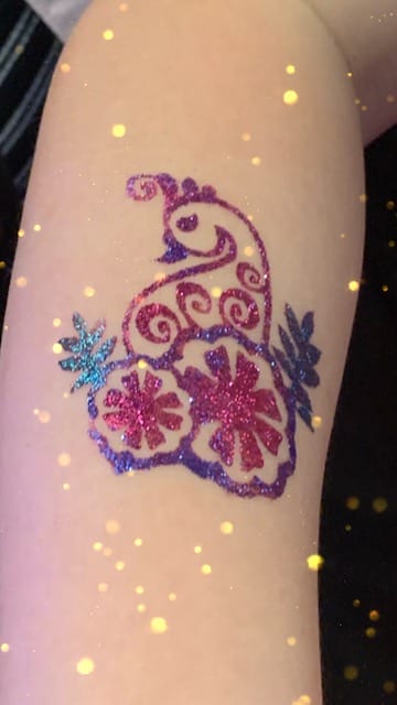 Sparkly glitter tattoo on arm with a snail design and decorative elements.