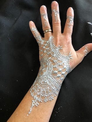 A hand adorned with silver glitter forming intricate henna-like patterns.