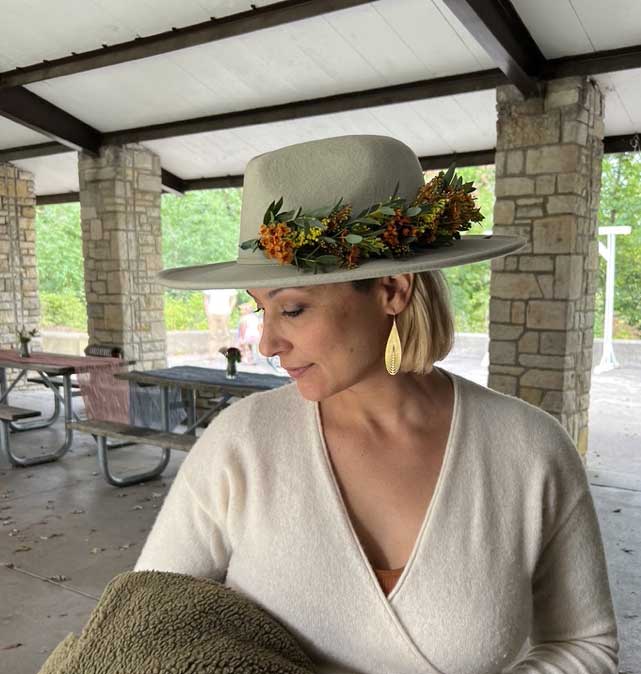 A woman wearing a white hat adorned with autumnal flowers and foliage.