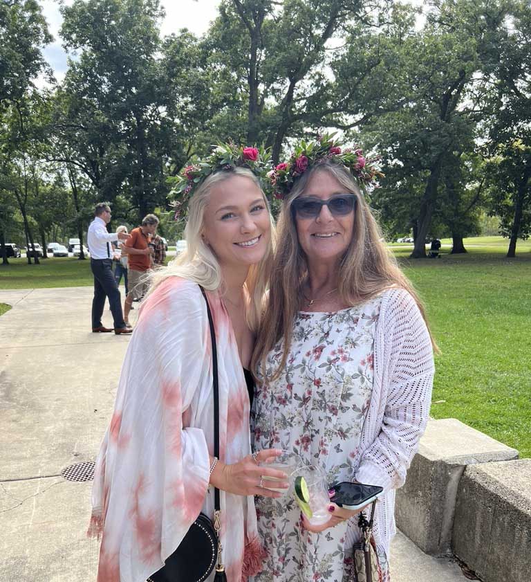 Two women wearing floral crowns and smiling outdoors at an event.