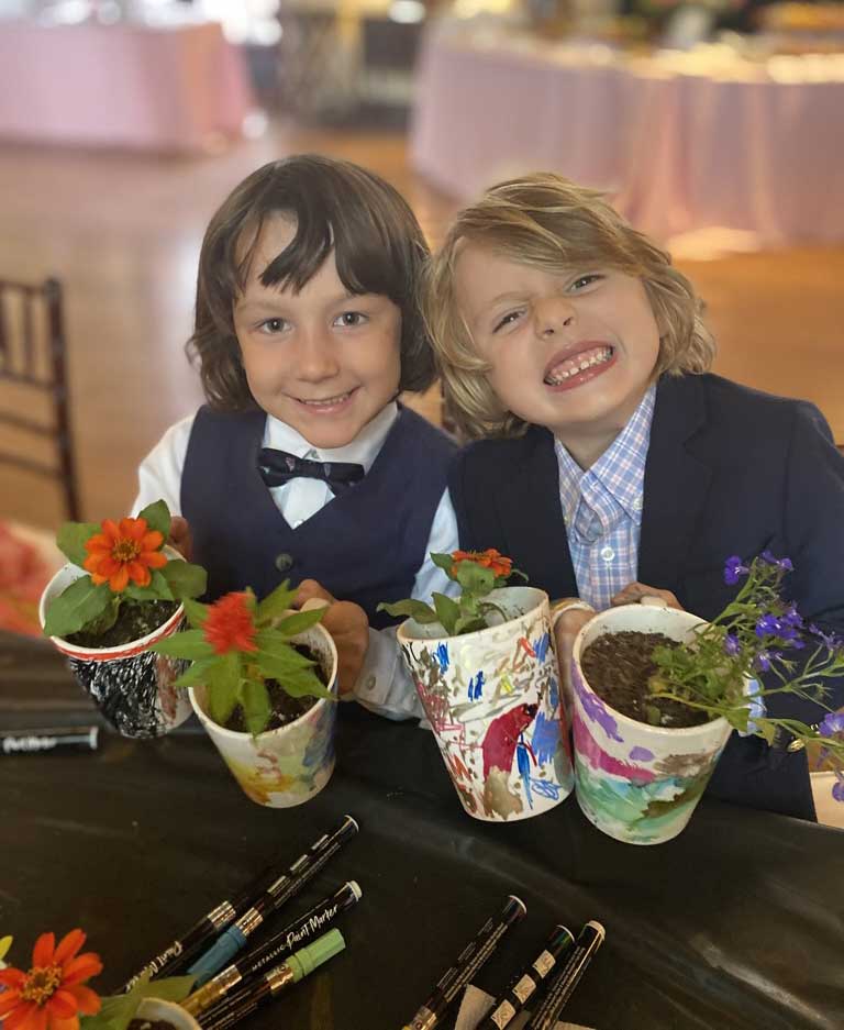 Two smiling children holding potted plants at an event.