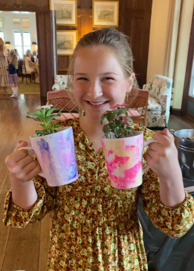 A smiling girl holding two painted mugs with plants inside.
