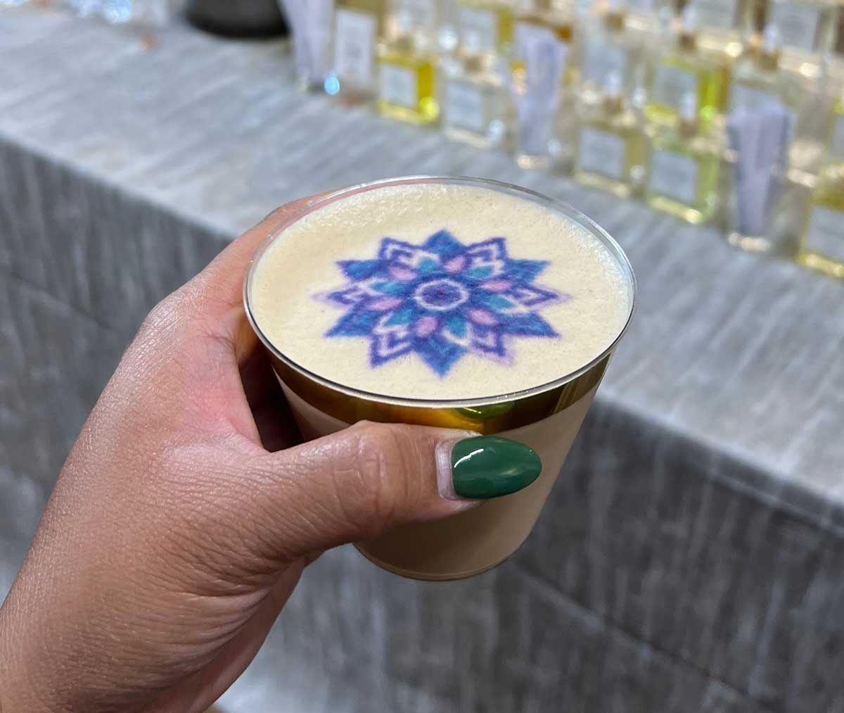 A hand holding a cup of coffee with latte art on a patterned surface.