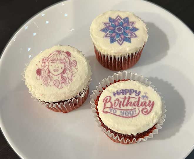 Three frosted cupcakes with decorative edible images, one reading "happy birthday to you," on a white plate.