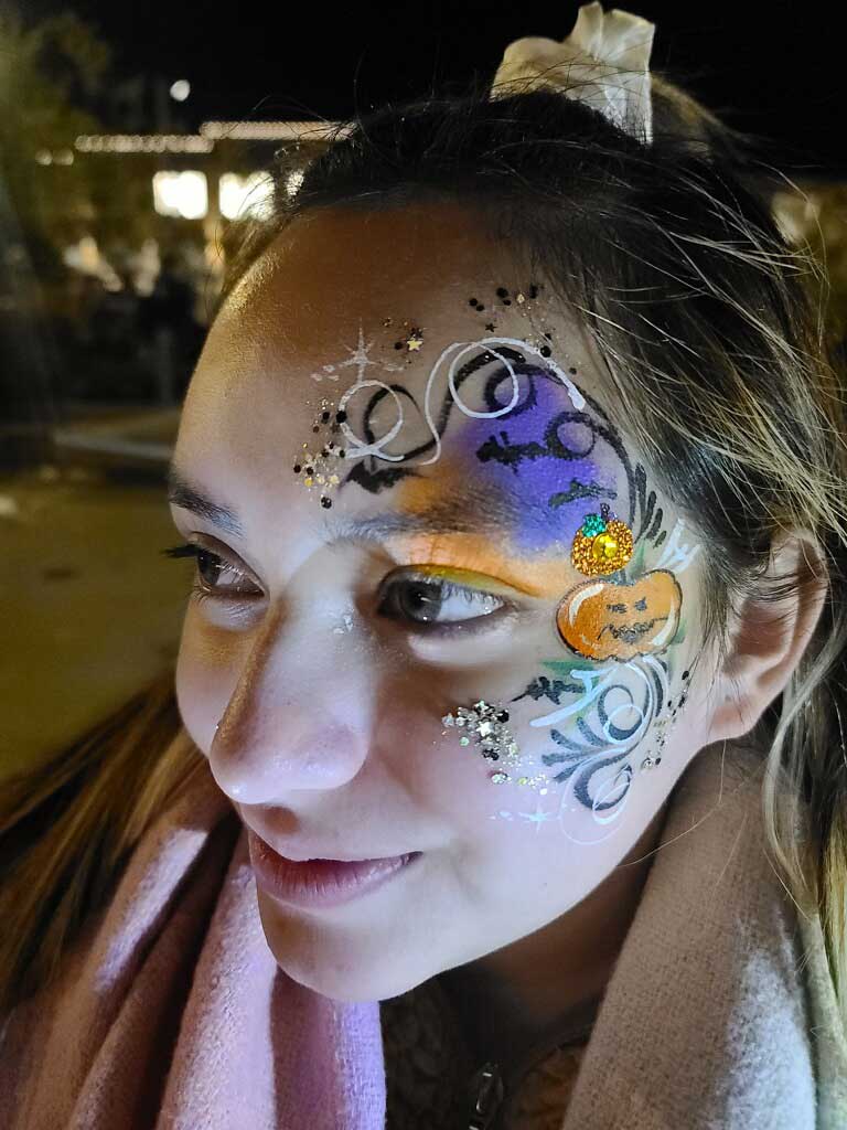 Woman with artistic face painting featuring a colorful design with swirls and sparkles.
