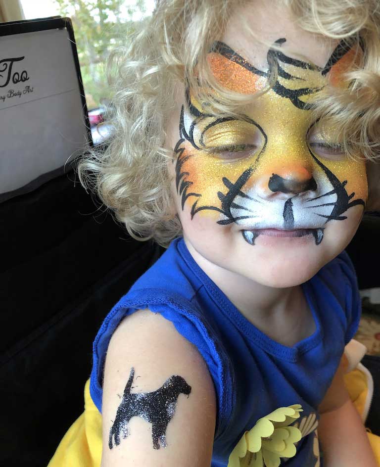 Child with face painted like a tiger and a temporary tattoo of the letter 'k' on the arm.