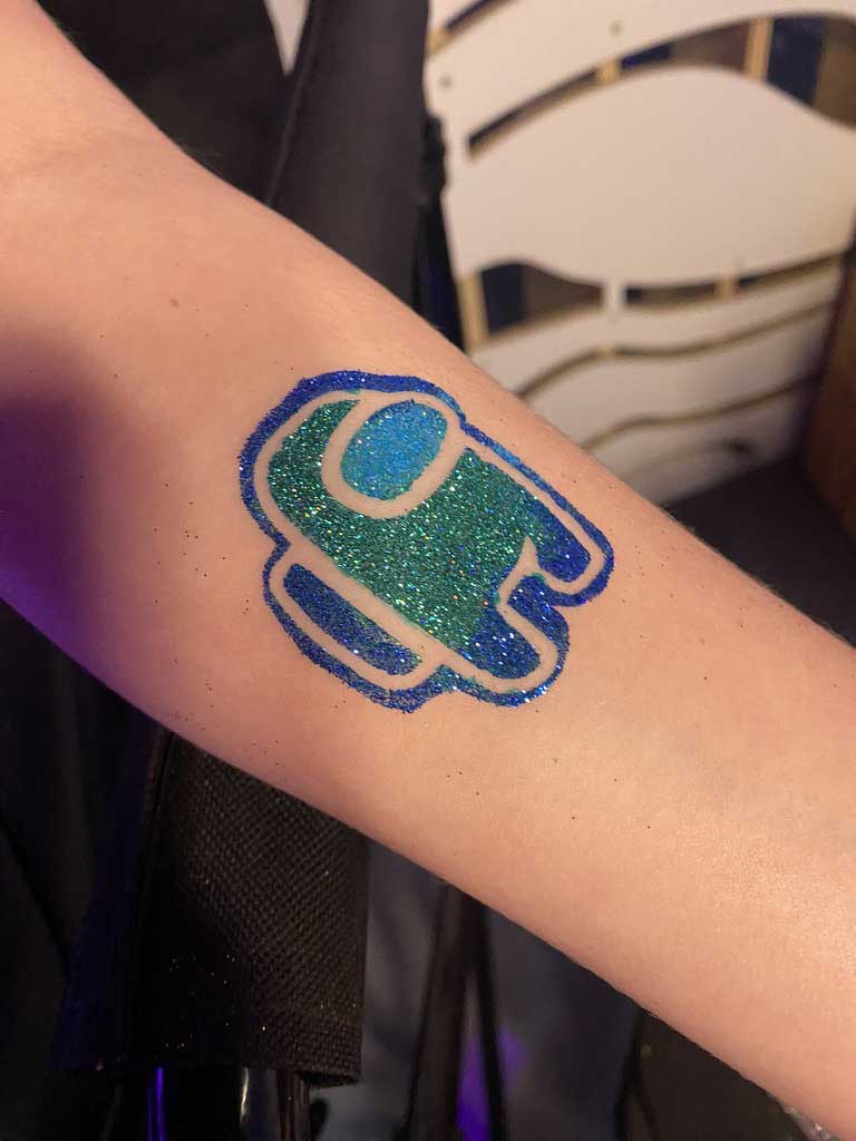 A glittery temporary tattoo of an among us character on a person's forearm.