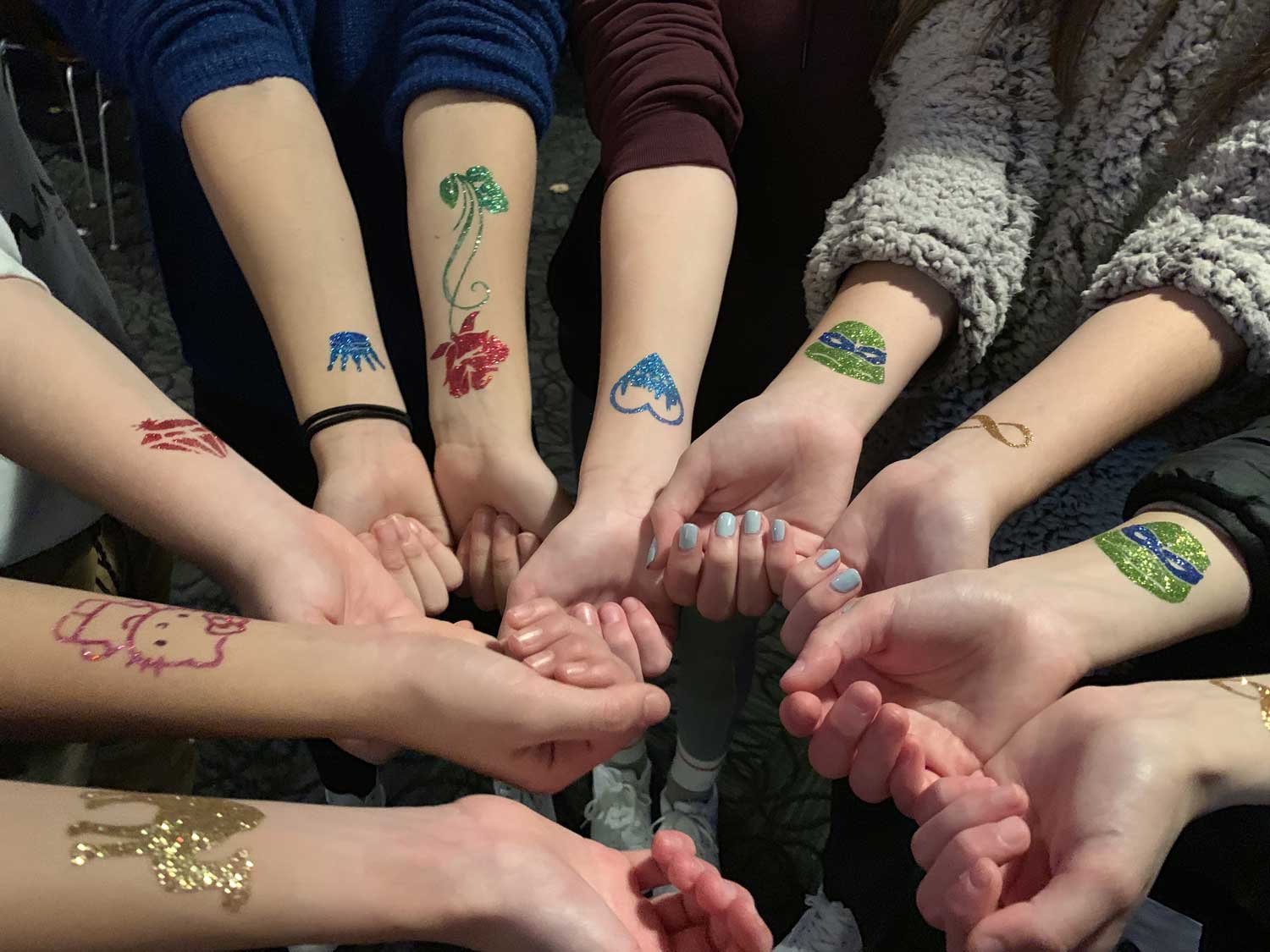 Group of people showing off their temporary tattoos while holding hands.
