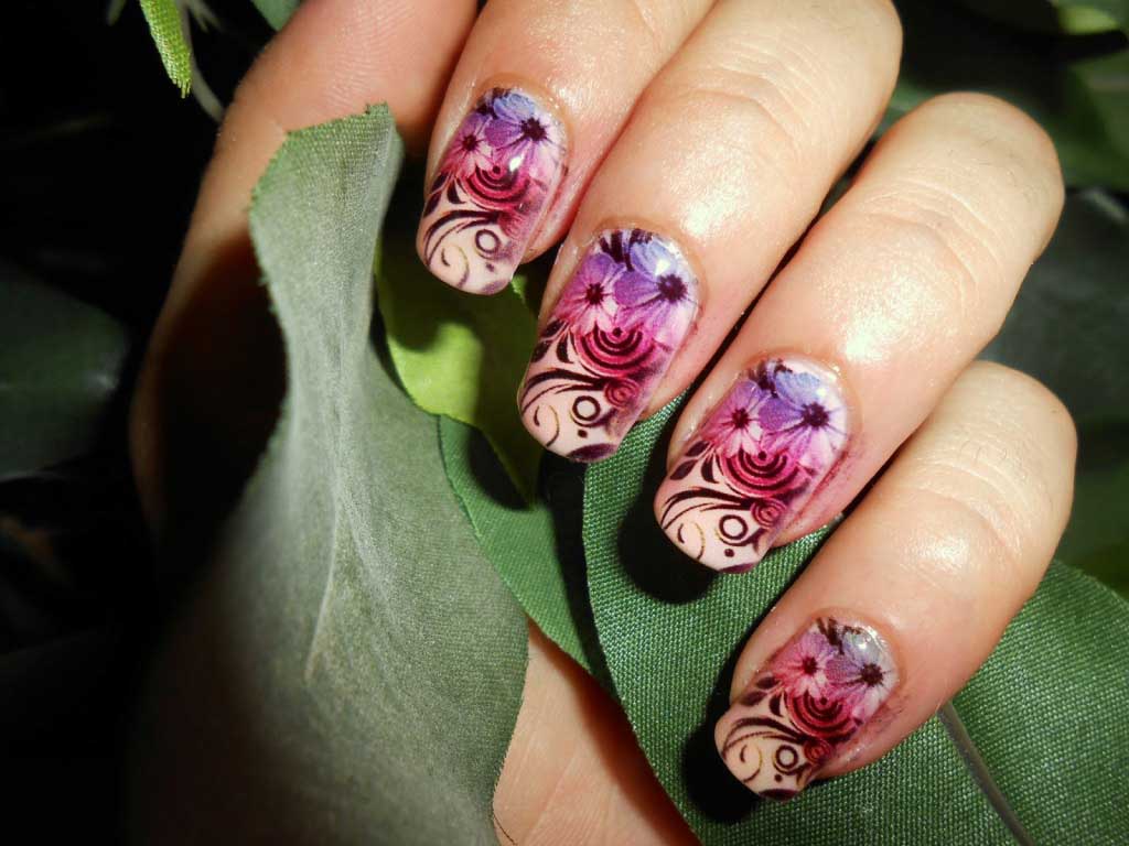 Close-up of a hand with floral nail art designs against green leaves.