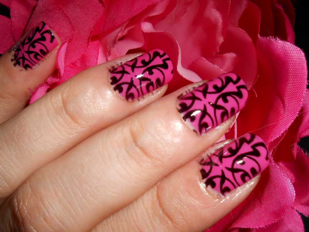Close-up of pink nails with black lace pattern design against a pink fabric background.