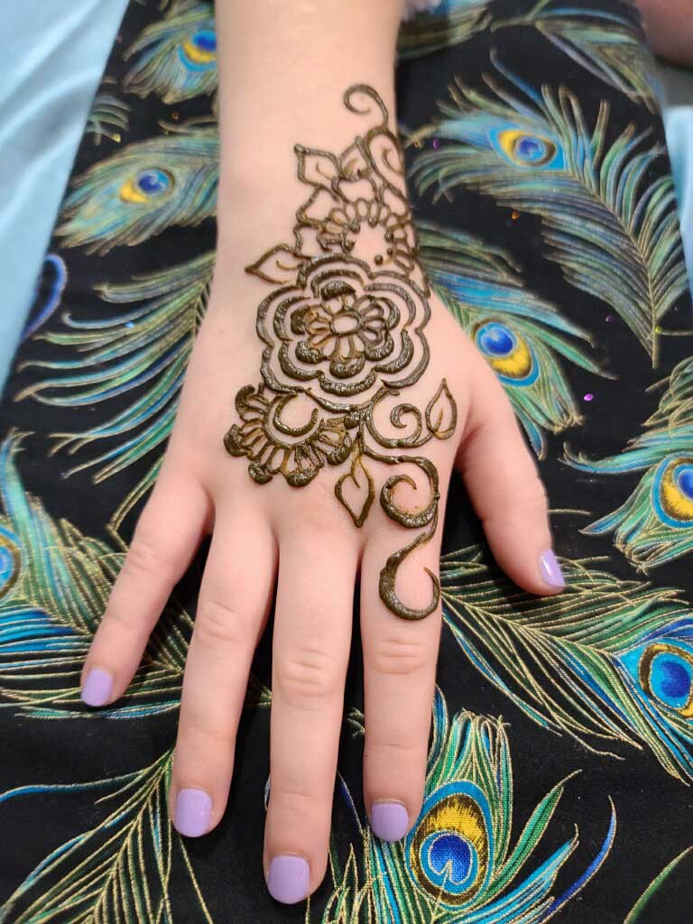 A hand displaying a brown henna design with a peacock feather pattern in the background.