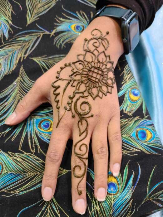 A hand with a floral henna design against a peacock feather patterned background.