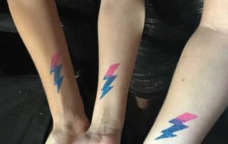 Four mitzvah attendees displaying their arms with matching lightning bolt tattoos of a custom bat or bar mitzvah logo