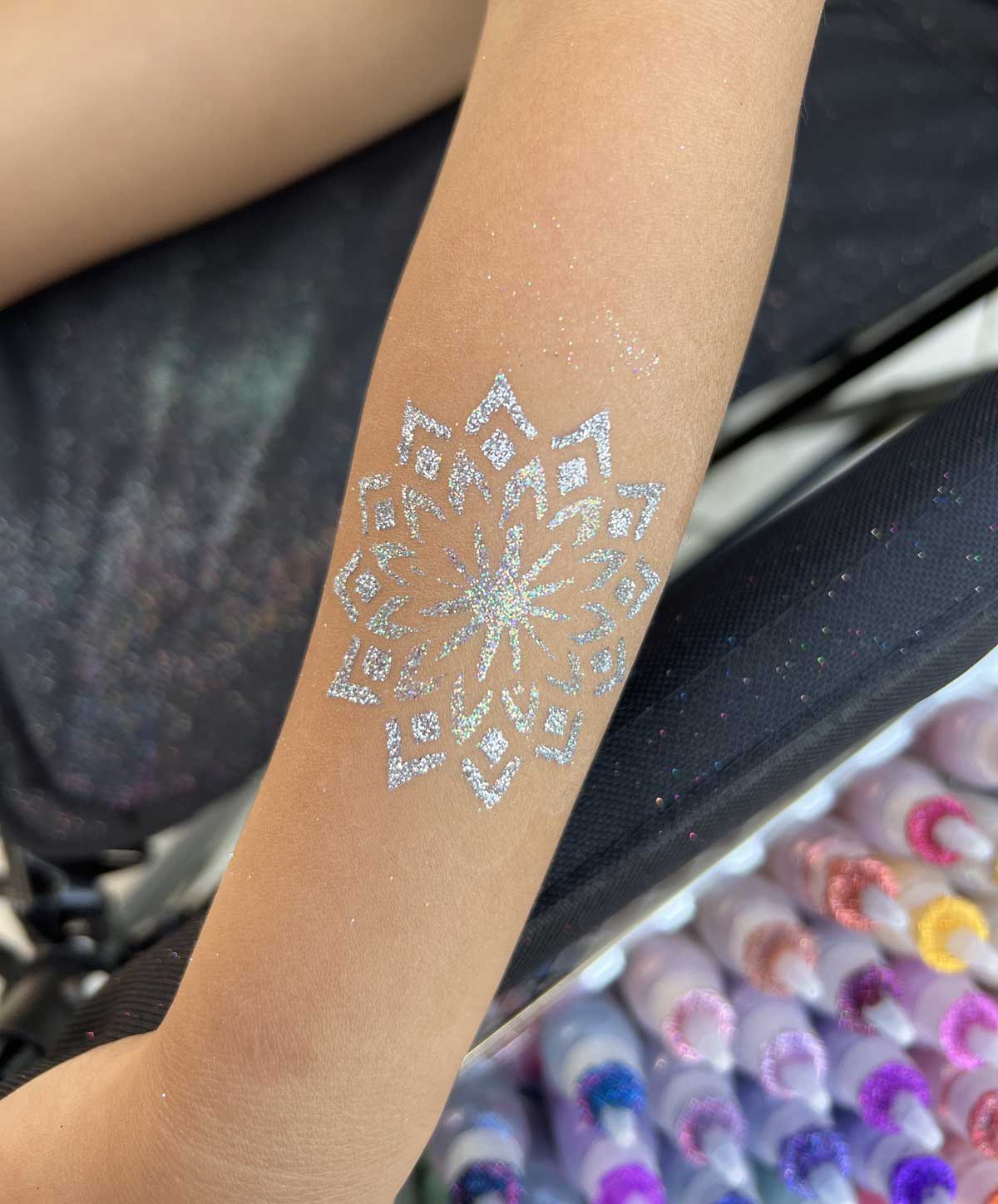 A glittering temporary tattoo of a mandala design on a person's arm.