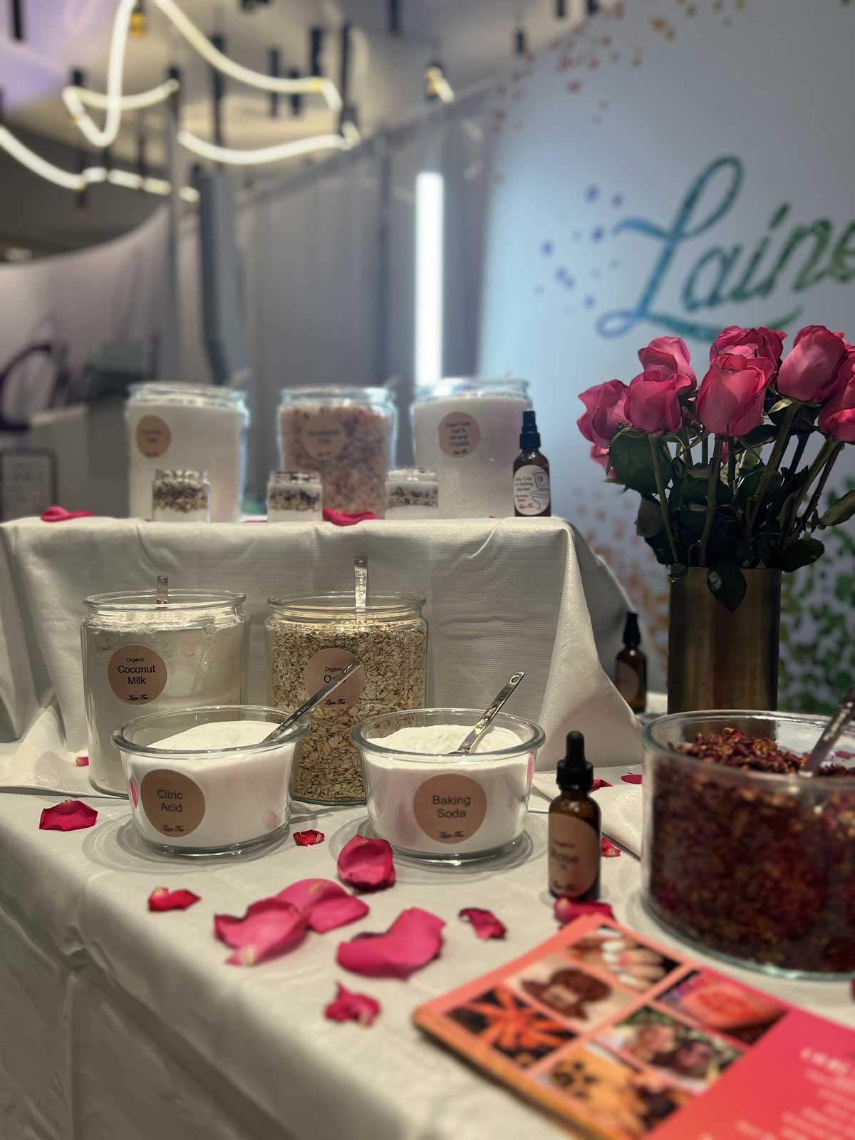 A display of beauty products with rose petals, various creams, and oils on a draped table at a promotional event.