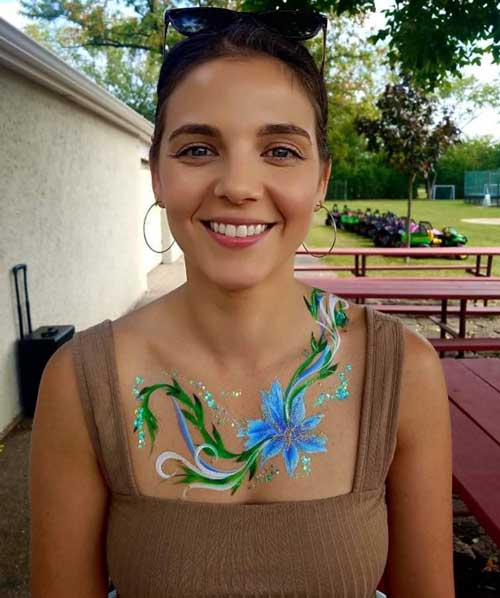 Woman smiling with face paint of a blue flower and green leaves on her chest.