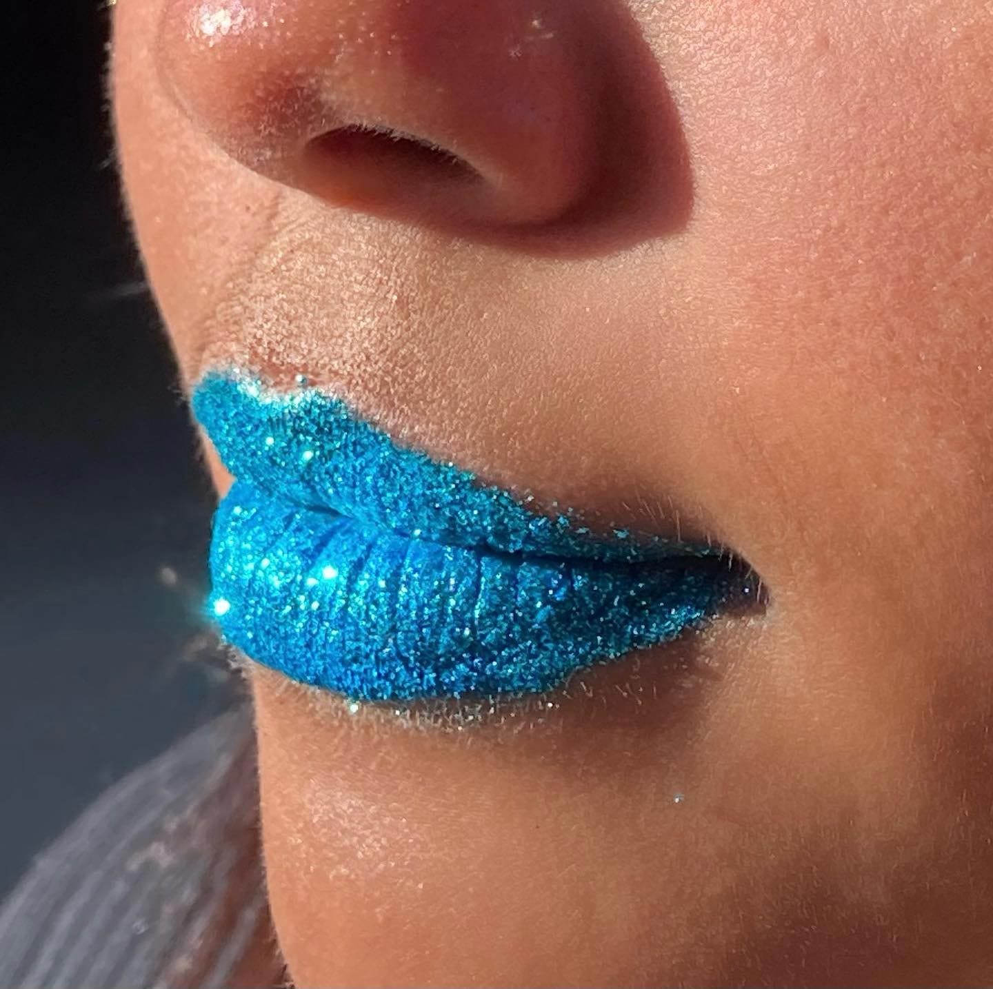 Close-up of shimmering blue lipstick on lips with sunlight highlighting the glitter.