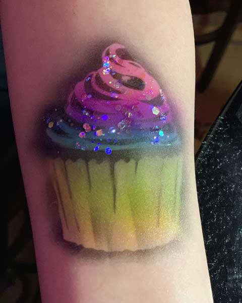 A colorful cupcake tattoo with sparkly details on someone's arm.