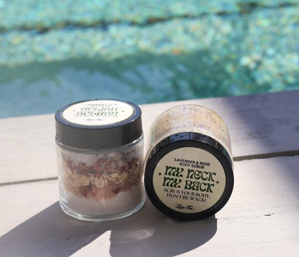 Two jars of body scrub placed on the edge of a pool with clear water in the background.