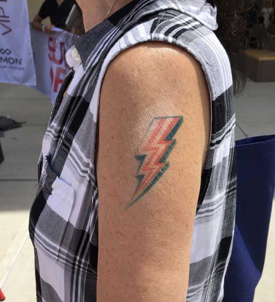 A person with a tattoo of a red and green lightning bolt on their upper arm.