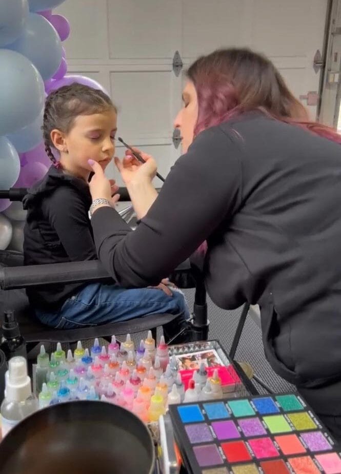 A child getting face paint applied by an artist with a palette of colorful options.