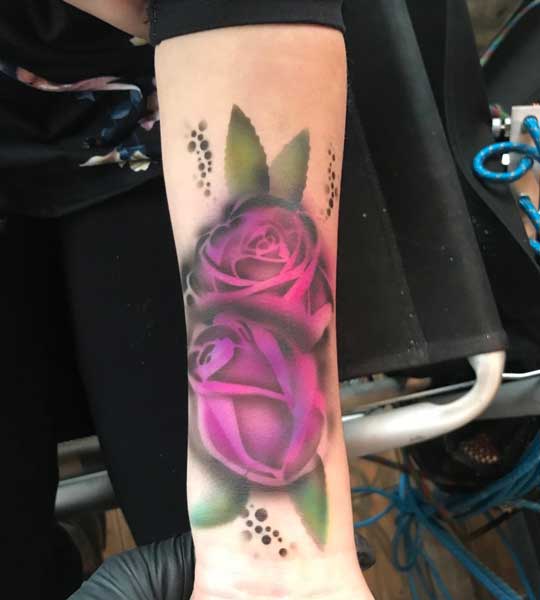 A close-up of a forearm with a realistic tattoo of purple roses.