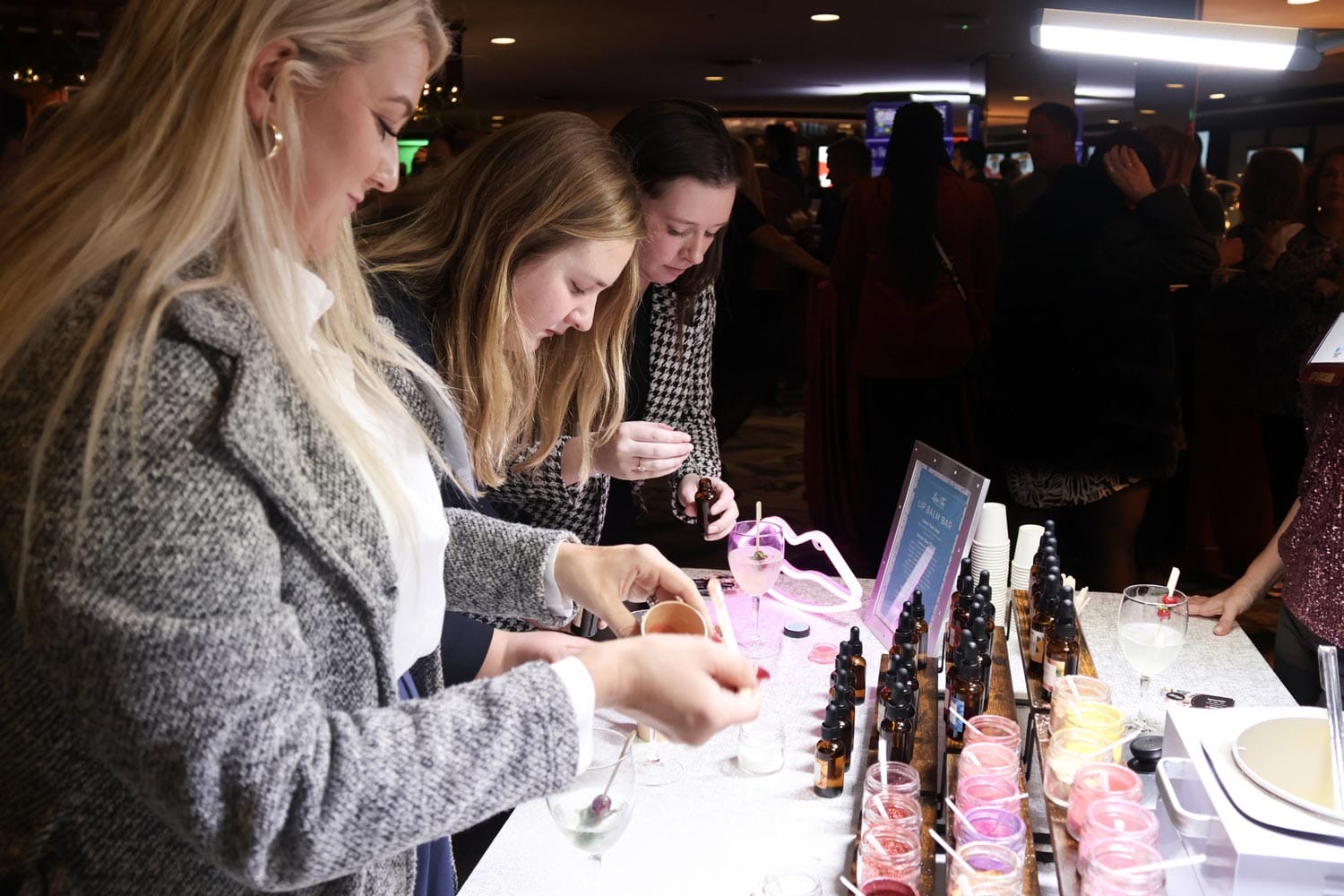Three women inspecting and selecting products at a display table during an indoor event.