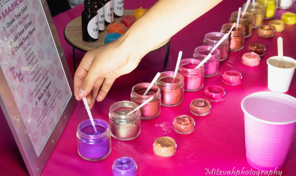 A hand selecting a brush from a colorful assortment of paint pots on a pink table.
