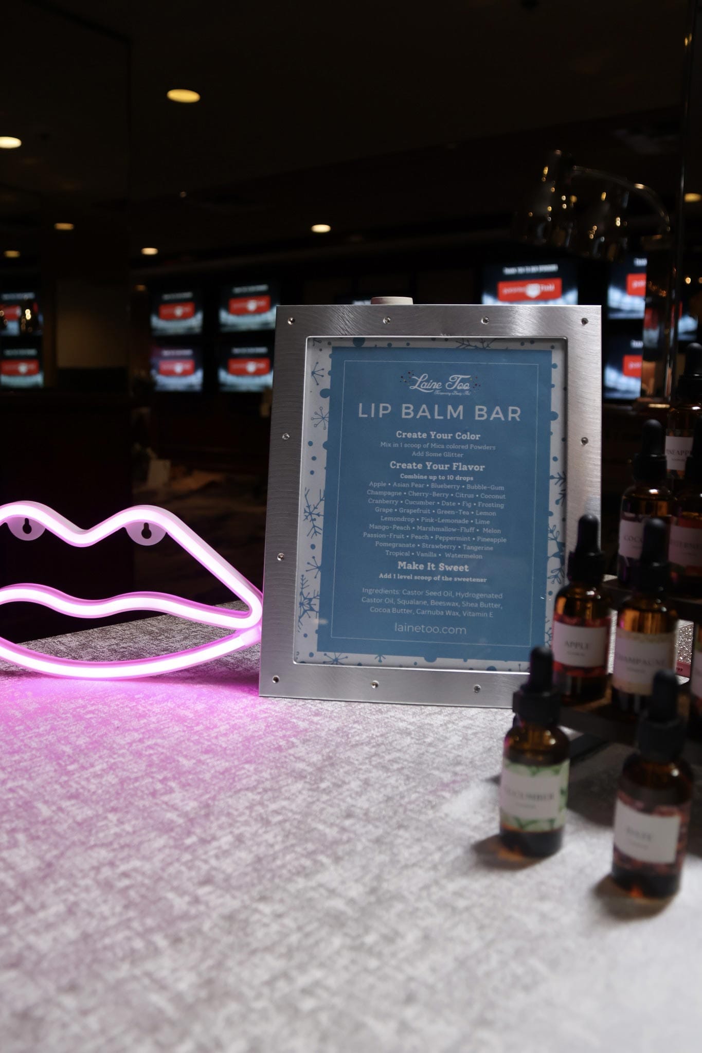 A tabletop display featuring a sign for a "lip balm bar" where customers can create their own lip balm flavors, accompanied by various bottles of ingredients.