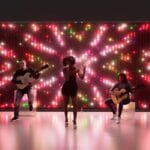 Colorful LED backdrop wall lit with pink, red and white lights behind a singer and two guitarists